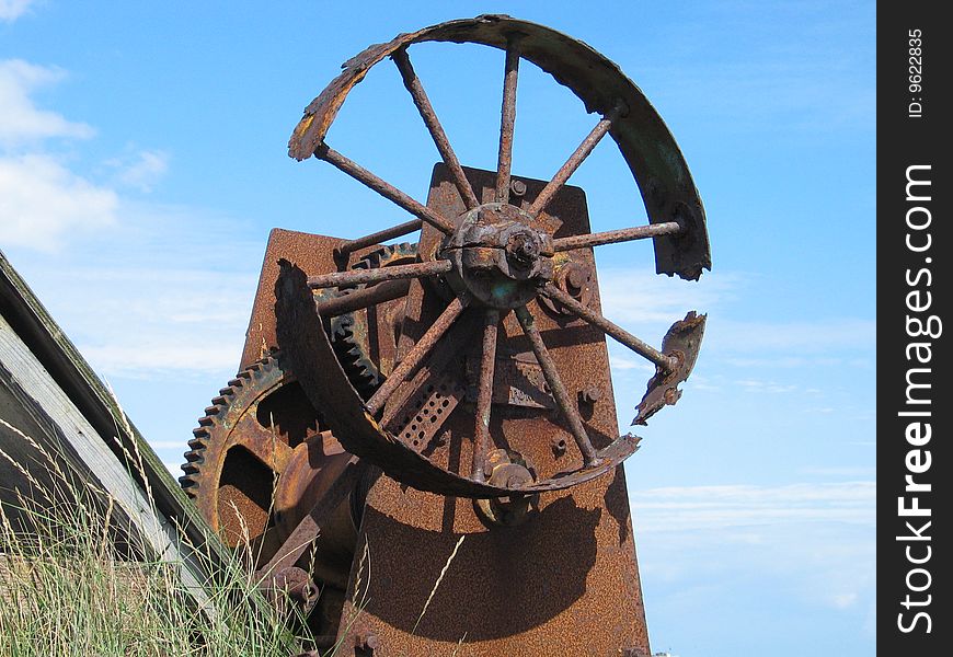 Rusty winding machinery on a beach against a blue sky. Rusty winding machinery on a beach against a blue sky