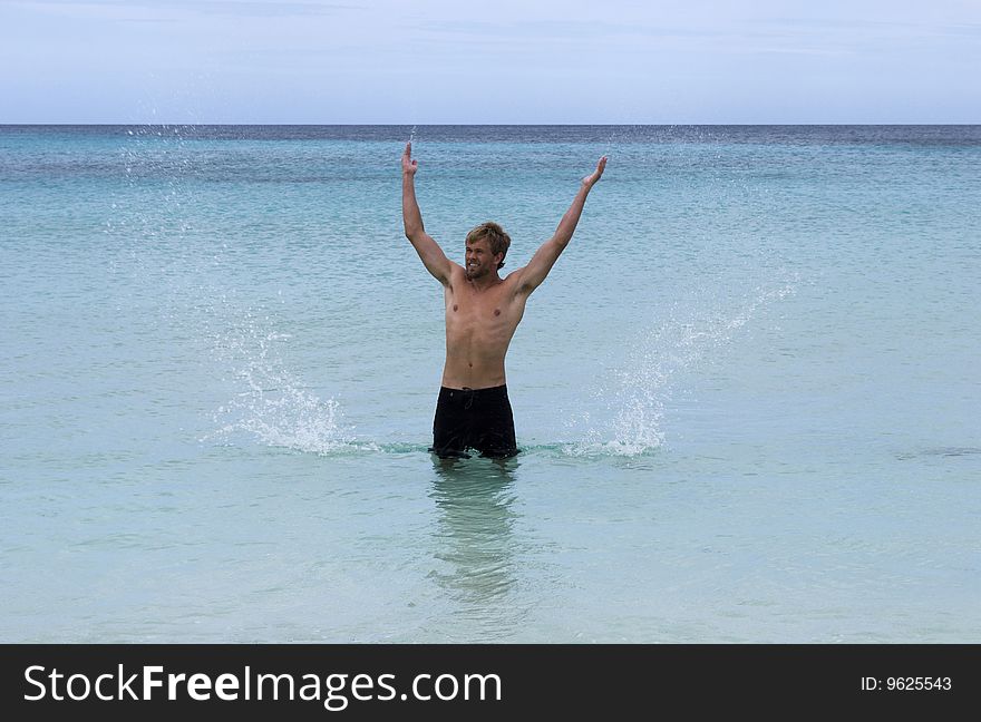 A man standing in the ocean sends sprays of water into the air. A man standing in the ocean sends sprays of water into the air.