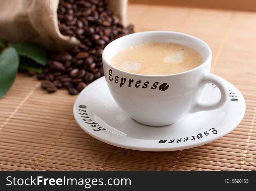 A bunch of coffee beans, falling out of a sack and a cup of fresh coffee on a wooden background