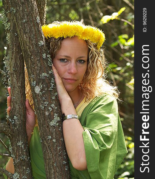 Curly girl with dandelion chain on head standing behind tree