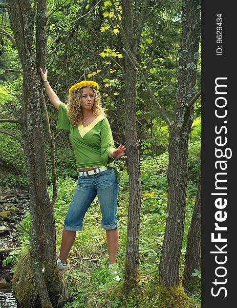 Curly girl with dandelion chain on head standing between trees