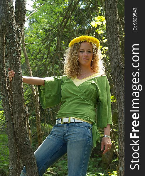 Curly girl with dandelion chain on head standing between trees
