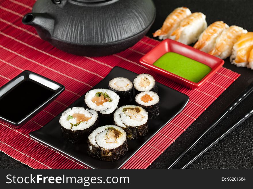 Sushi set and black teapot on red mat and black table