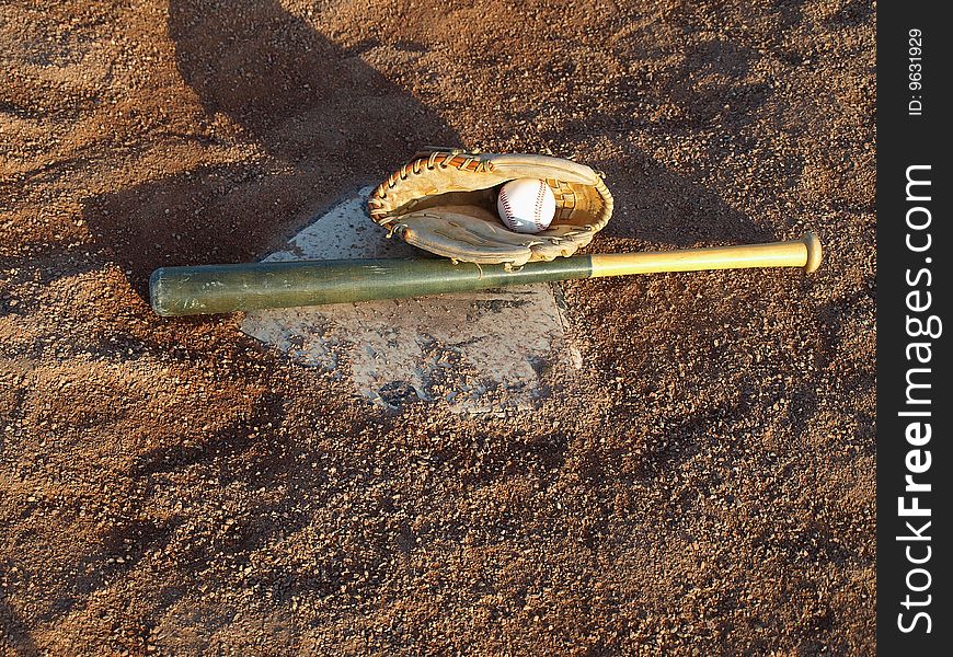 This bat,glove and ball are waiting on home base for the big game,with crushed shale for ground cover there is no mud on a rainy day. This bat,glove and ball are waiting on home base for the big game,with crushed shale for ground cover there is no mud on a rainy day.