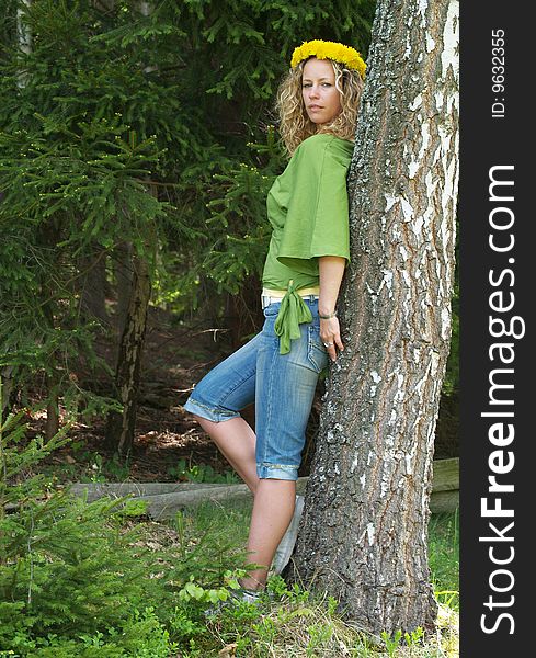 Curly girl with dandelion chain on head standing by birch tree