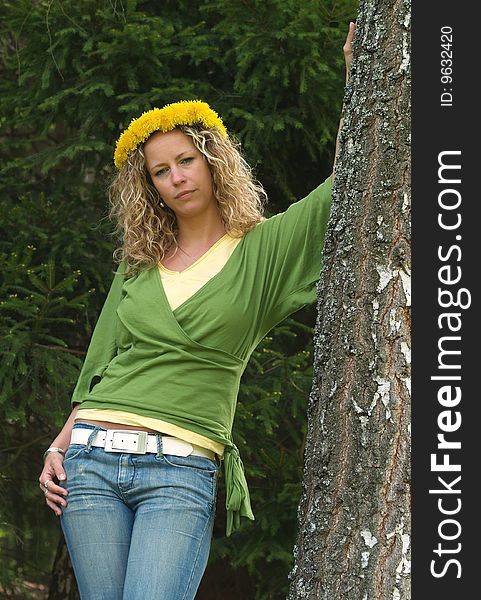 Curly girl with dandelion chain on head standing by birch tree