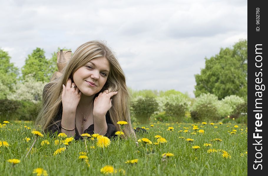 Young adult beautiful girl lying on the grass with dandelion