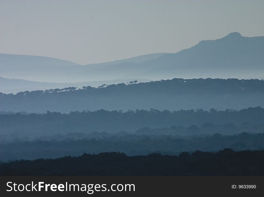 Early morning day break at the Huluhluwe-Umfolozi Game Reserve, South Africa, showing misty hills and silhouettes of trees. Early morning day break at the Huluhluwe-Umfolozi Game Reserve, South Africa, showing misty hills and silhouettes of trees