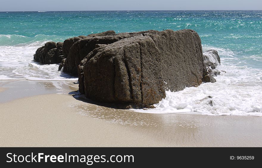 A large rock on a pale sandy beach with white surf around. A large rock on a pale sandy beach with white surf around.