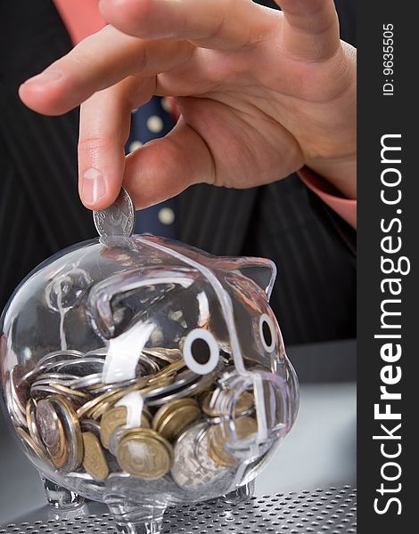 Businessman's hand inserting coin into transparent piggy bank