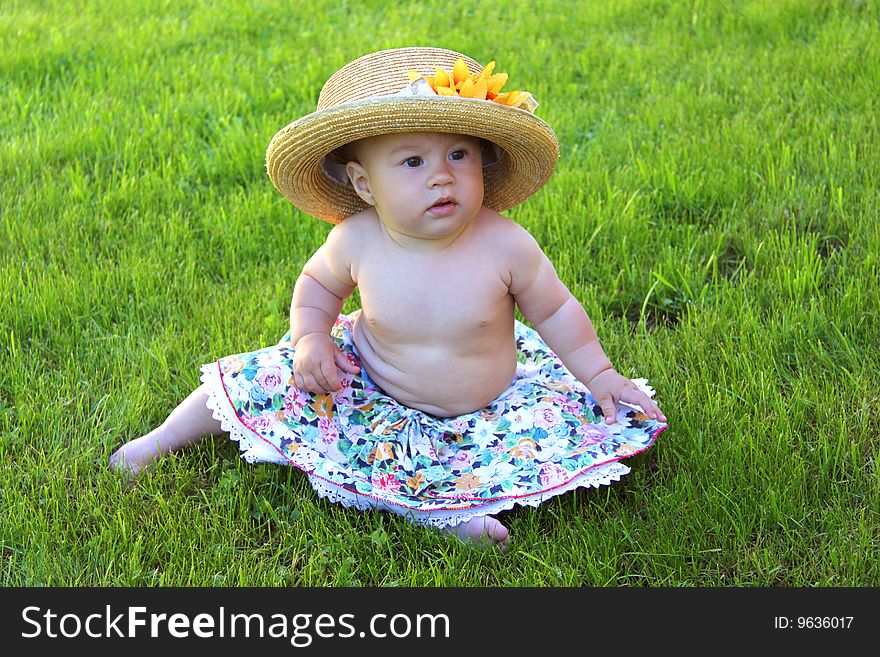 Baby girl wearing big hat sits on green grass