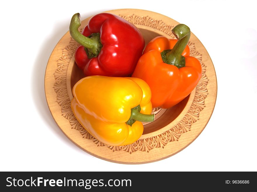 Orange, yellow and red pepper on a wooden plate.