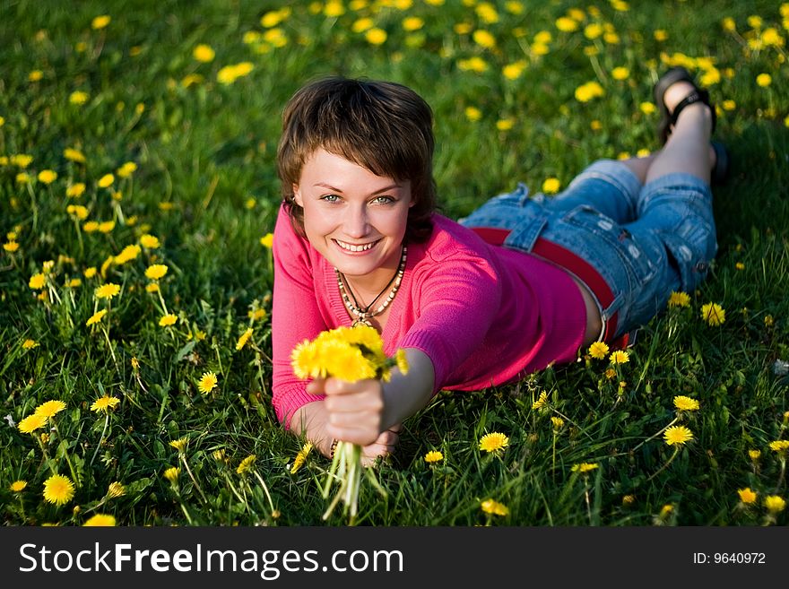 A young cheerful woman having fun on a dandelions glade