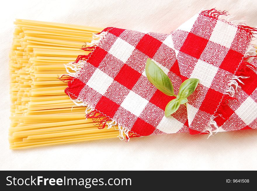 Spaghetti and basil covered by red and white checked napkin