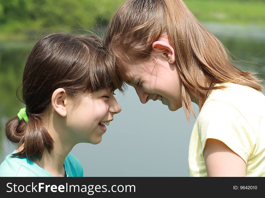 Close-up of two young smiling girls standing face-to-face with closed eyes on nature background. Close-up of two young smiling girls standing face-to-face with closed eyes on nature background