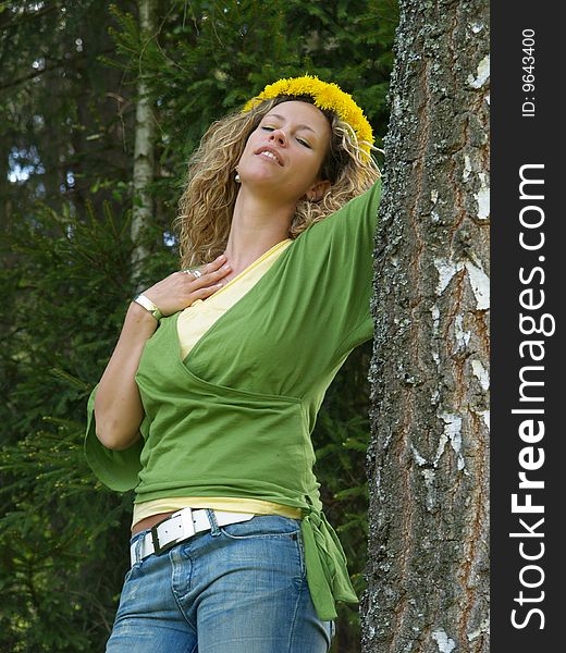 Curly girl with dandelion chain on head standing by birch tree