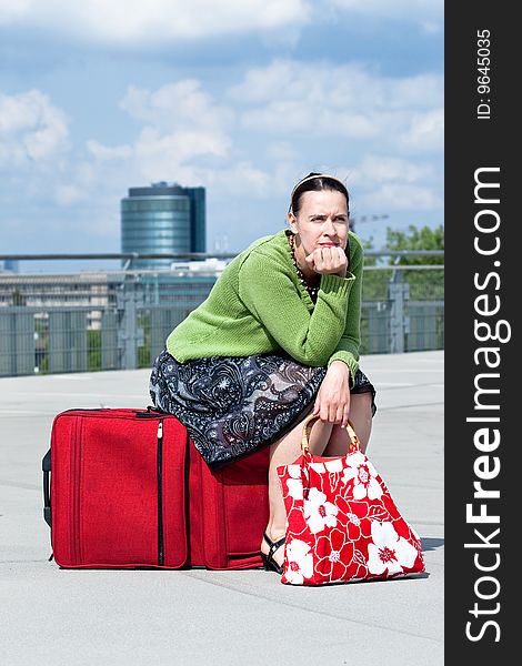 A woman sitting on a suitcase in an urban setting. A woman sitting on a suitcase in an urban setting.