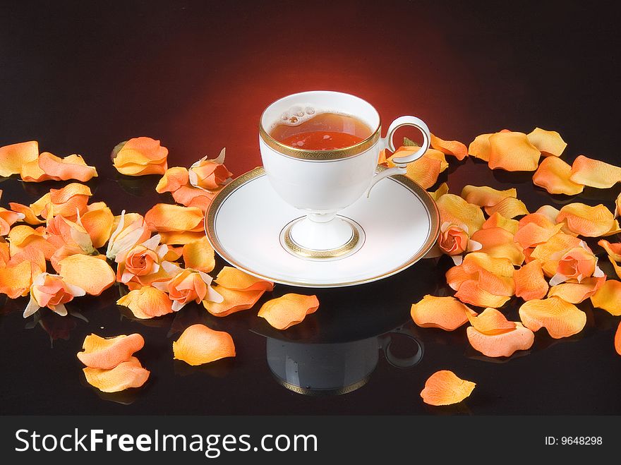 Cup of tea and rose petals on black glass background. Cup of tea and rose petals on black glass background