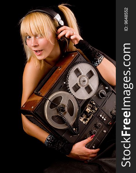A young beautiful blonde with an old tape in the hands and the headphones on a black background. A young beautiful blonde with an old tape in the hands and the headphones on a black background