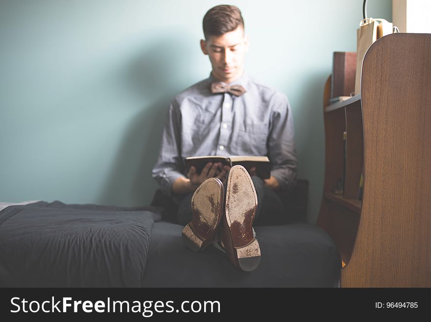 Man in Purple Dress Shirt Sitting on Bed Holding Books