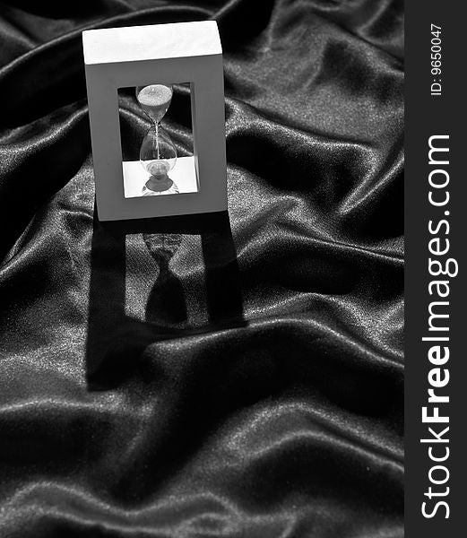 Still life of a backlighted hourglass on a crumpled black cloth, in black and white. Still life of a backlighted hourglass on a crumpled black cloth, in black and white