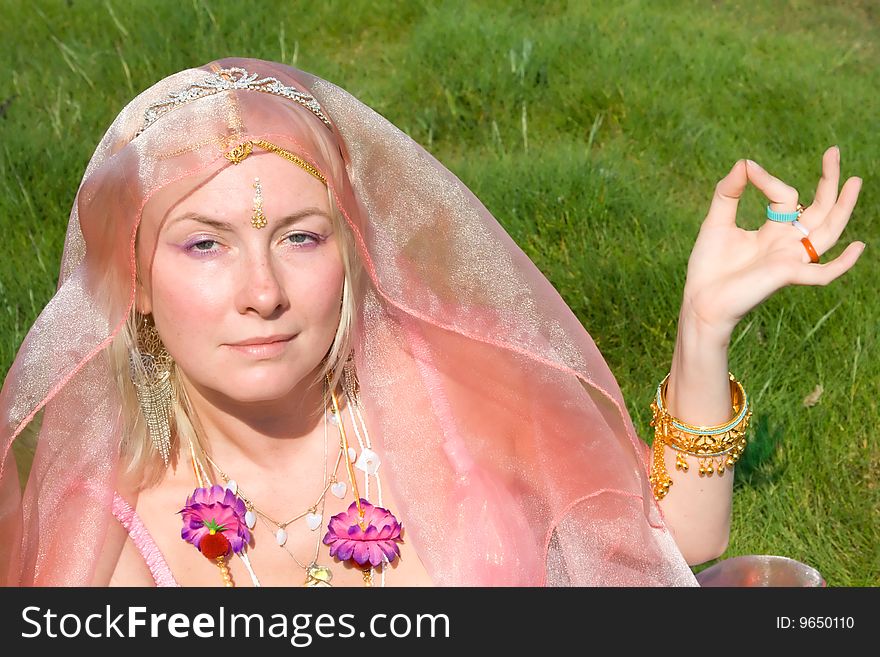 A woman in pink asian dress in meditation on a green grass