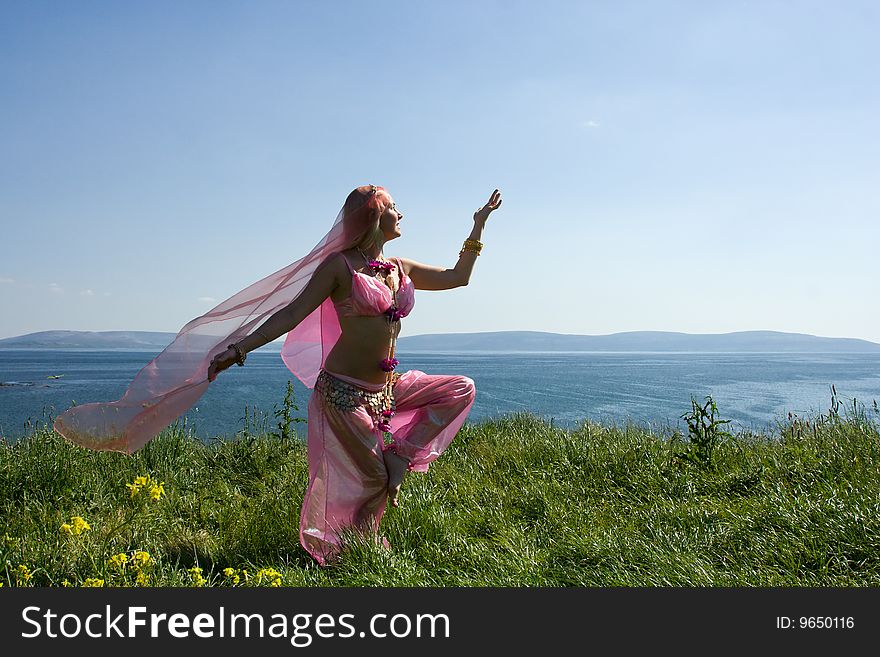 A woman in a pink asian dress dancing at the ocean coast. A woman in a pink asian dress dancing at the ocean coast