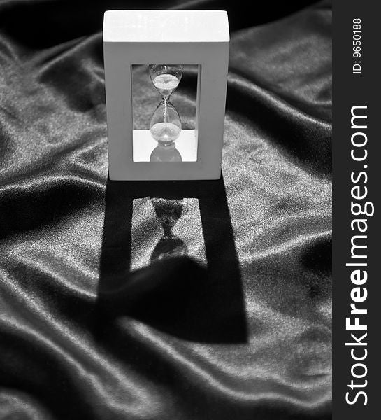 Still life of a backlighted hourglass on a crumpled black cloth, in black and white. Still life of a backlighted hourglass on a crumpled black cloth, in black and white