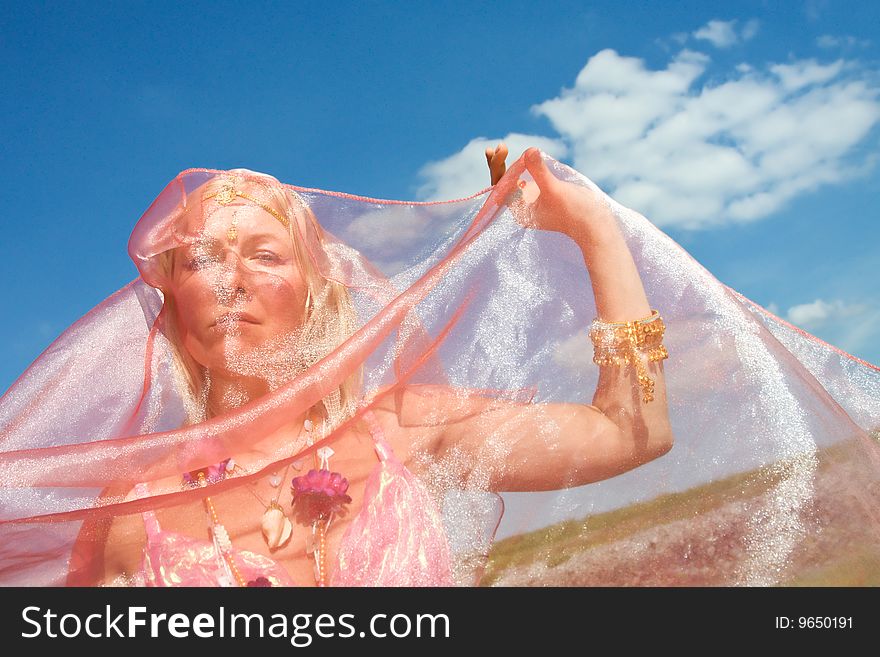 A woman cover her face with a pink dress and ablue sky with clouds