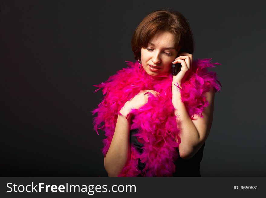 Beautiful woman in pink feathers speaks on phone. Close-up view. Beautiful woman in pink feathers speaks on phone. Close-up view