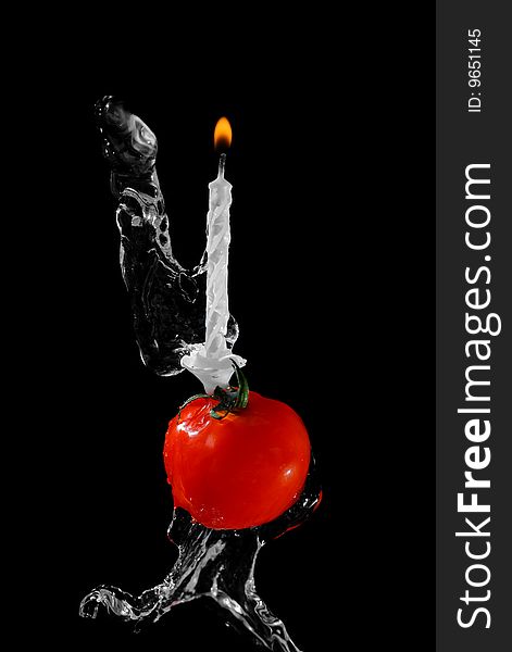 Tomato and candle in water stream on black background