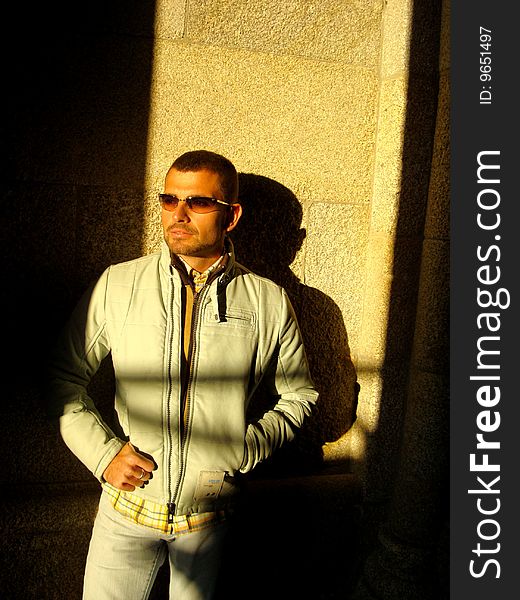 Male model with sunglasses on a brick stone wall half in the sun, half in the shadow. Male model with sunglasses on a brick stone wall half in the sun, half in the shadow