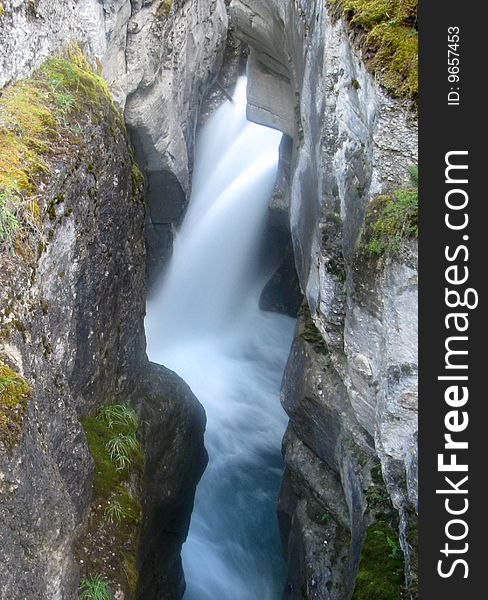 A blue and white waterfall cascading into a narrow canyon.