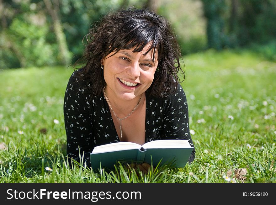 Smiling young woman lying on a flowery meadow reads a book. Smiling young woman lying on a flowery meadow reads a book