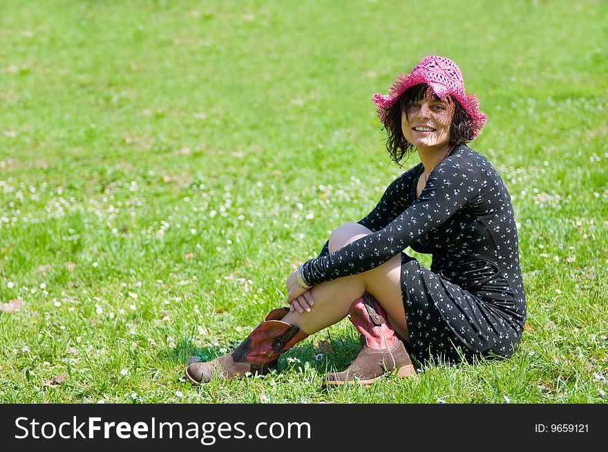 Young woman smiling and sitting on a flowery meadow, wearing purple hat. Young woman smiling and sitting on a flowery meadow, wearing purple hat