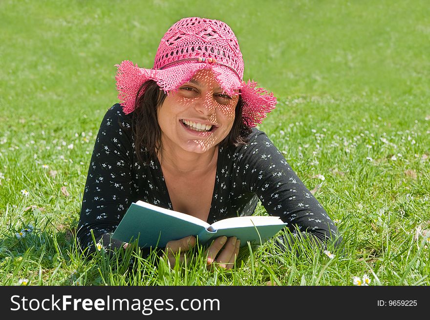 Smiling young woman lying on a flowery meadow reads a book. Smiling young woman lying on a flowery meadow reads a book