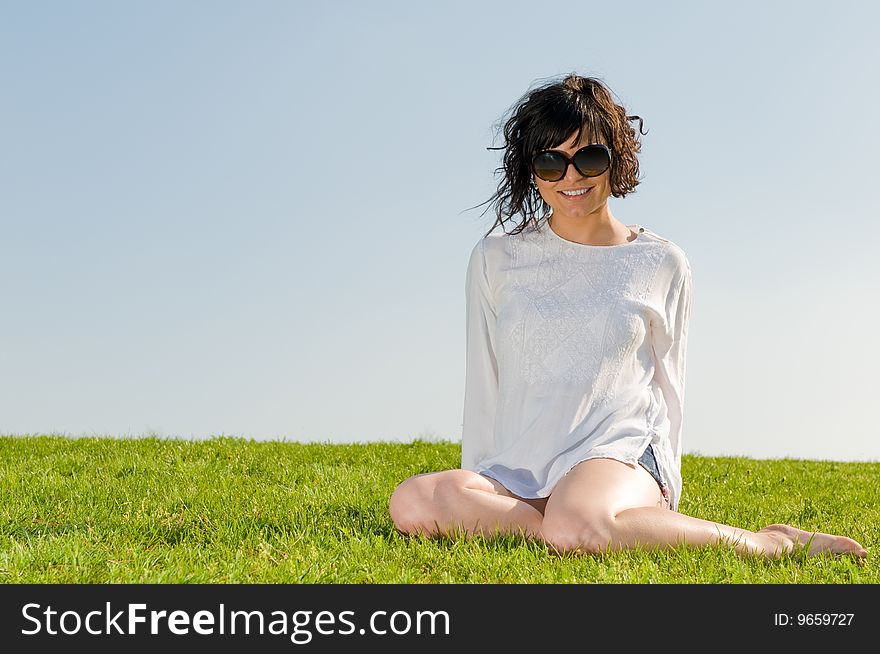 Smiling girl dressed in white sitting on the grass with blue sky. Smiling girl dressed in white sitting on the grass with blue sky