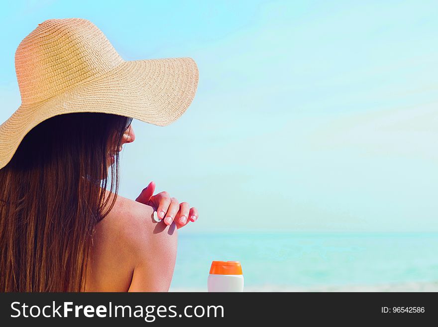 Brunette putting sunscreen on her shoulder on beach