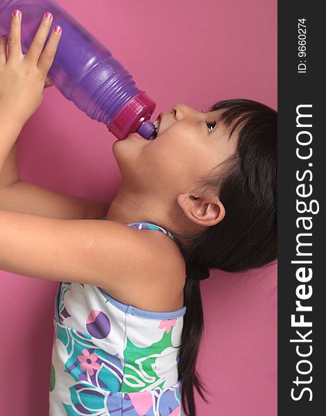 Asian Chinese Girl drinking from a reuseable water bottle with pink back round with head tilted back. Asian Chinese Girl drinking from a reuseable water bottle with pink back round with head tilted back