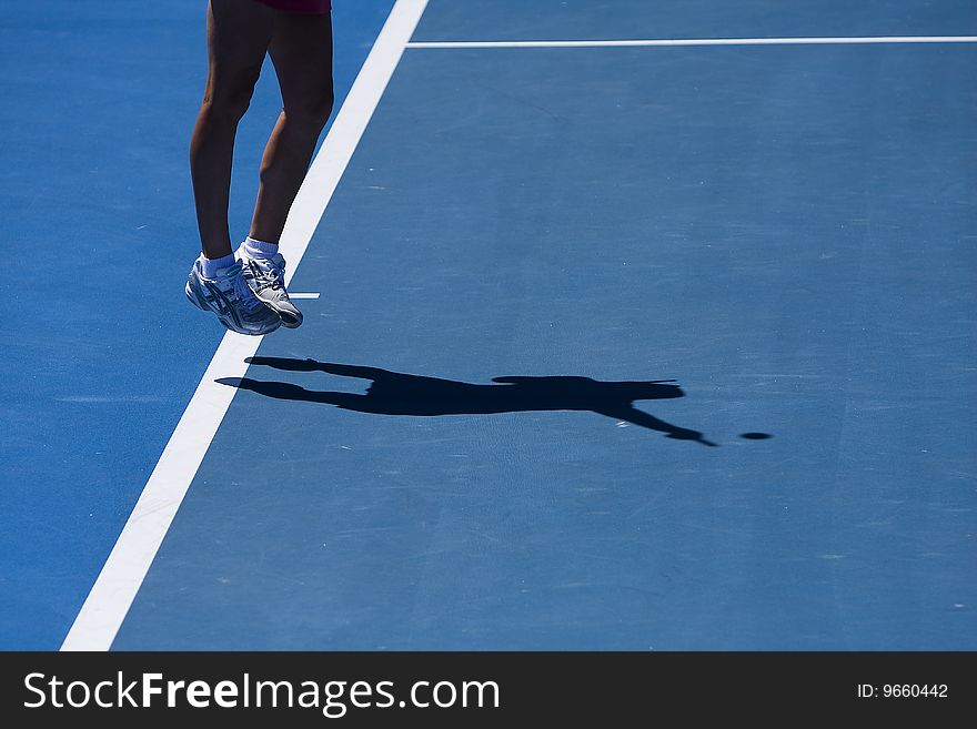 A tennis player at a tournament serving, shown by the shadow. A tennis player at a tournament serving, shown by the shadow.