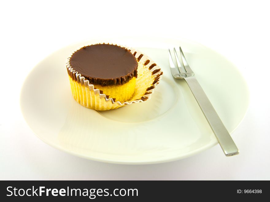 A delicious looking cup cake resting on a white plate with a fork on a plain background. A delicious looking cup cake resting on a white plate with a fork on a plain background