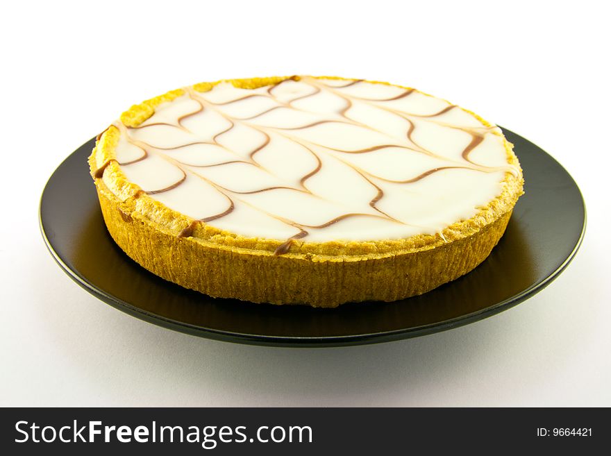 Delicious looking iced bakewell tart on a black plate with a plain background