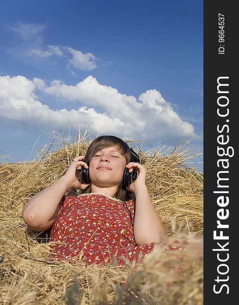 Young girl listenning to music in a stack of hay