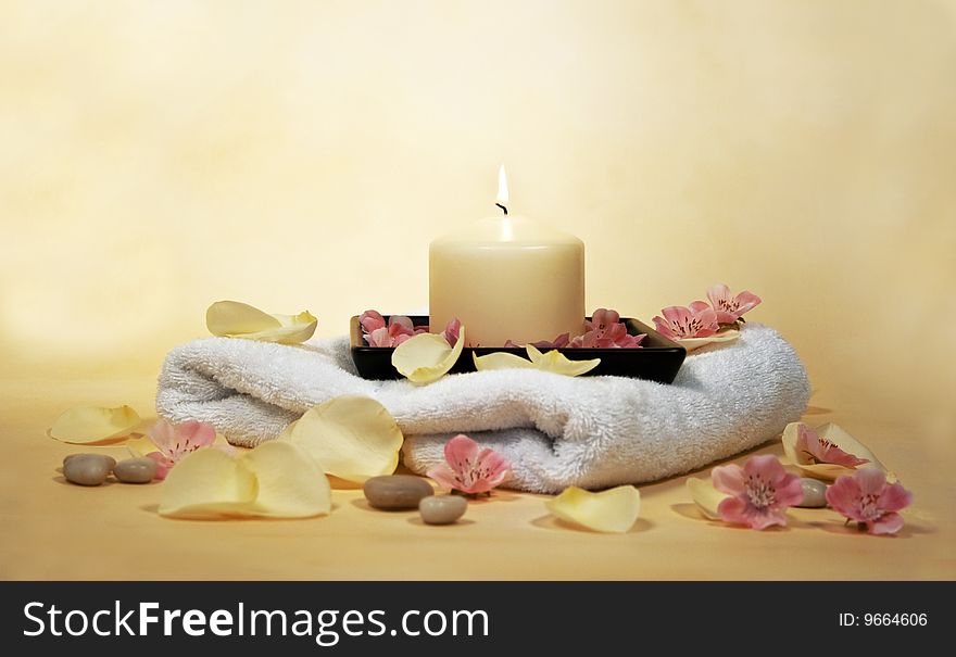 White towel with yellow candle and rose leaves and little stones. White towel with yellow candle and rose leaves and little stones