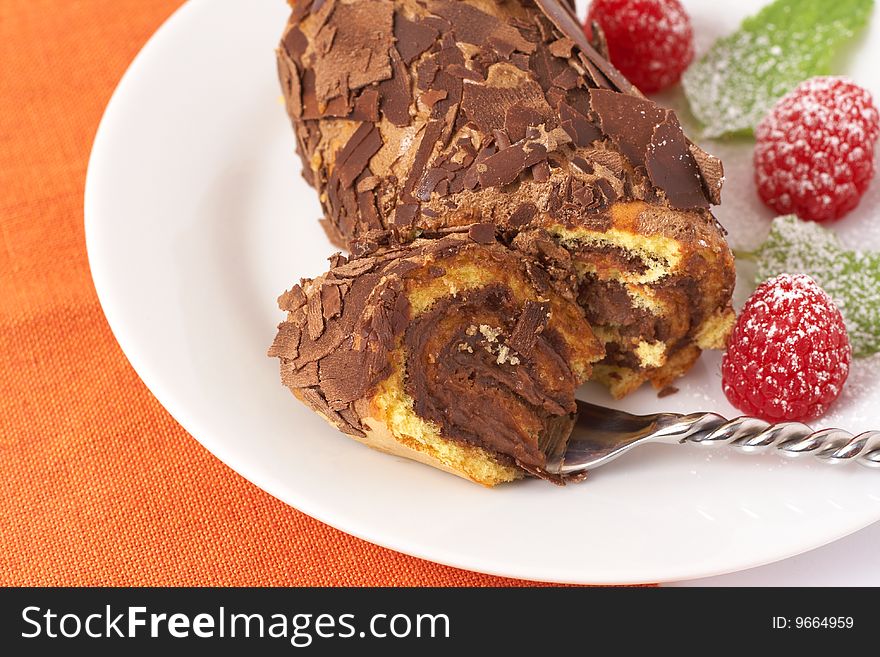 Miniature chocolate swiss roll cake served on a plate with mint leaves and raspberries on orange background