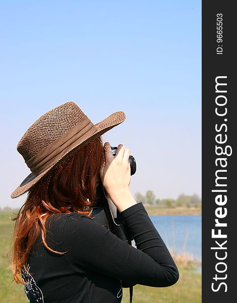 The girl in the hat on  the bank of the lake with camera. The girl in the hat on  the bank of the lake with camera