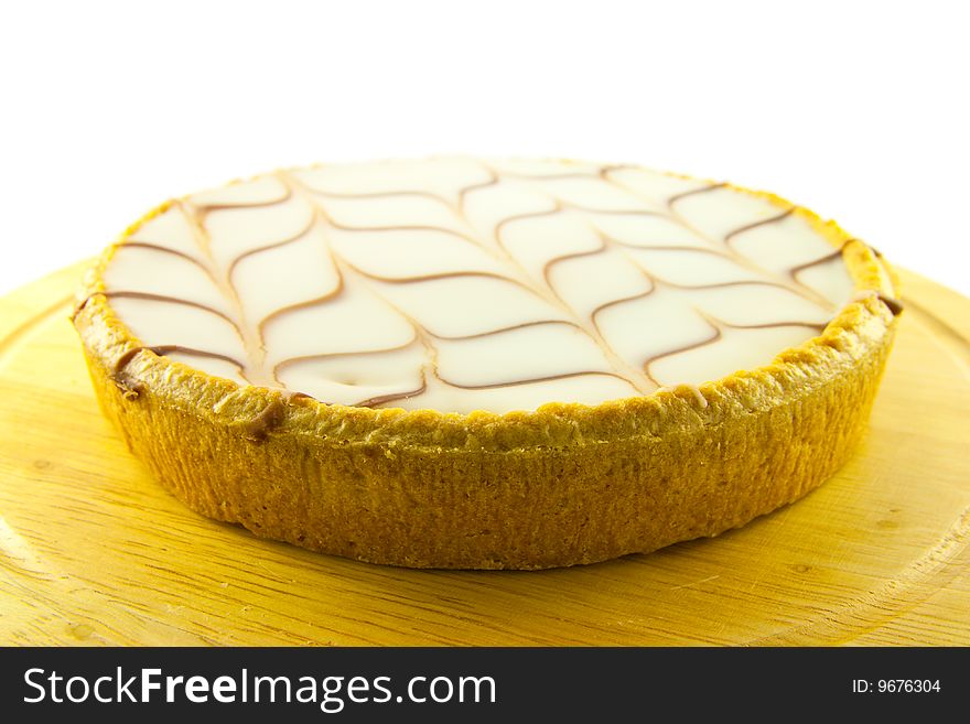 Delicious looking iced bakewell tart on a wooden platter with a plain background