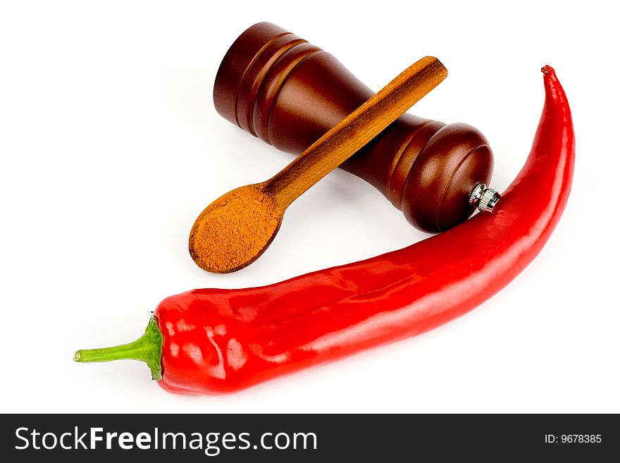 A composition of a pod of red chile pepper , a wooden hand mill for grinding and a wooden spoonful of ground red  pepper on a white background. A composition of a pod of red chile pepper , a wooden hand mill for grinding and a wooden spoonful of ground red  pepper on a white background