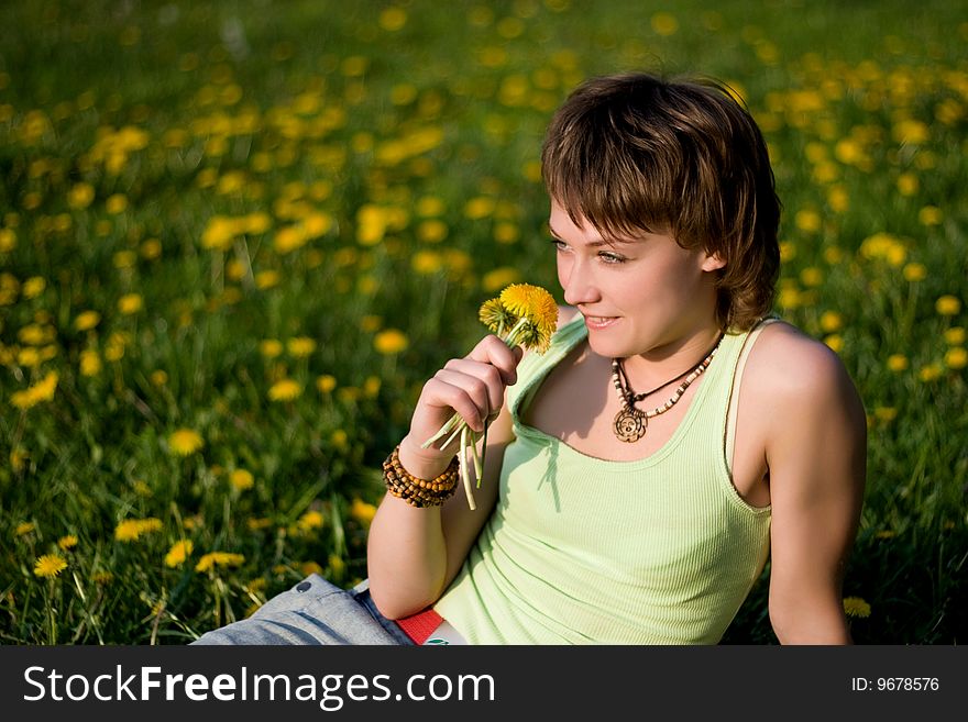 A young cheerful woman having fun on a dandelions glade