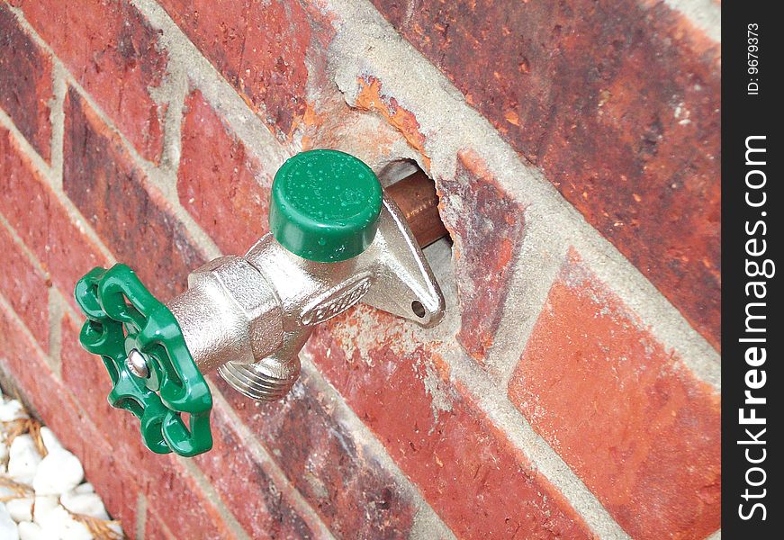 Green handled water spigot attached to a red-brick building. Green handled water spigot attached to a red-brick building.